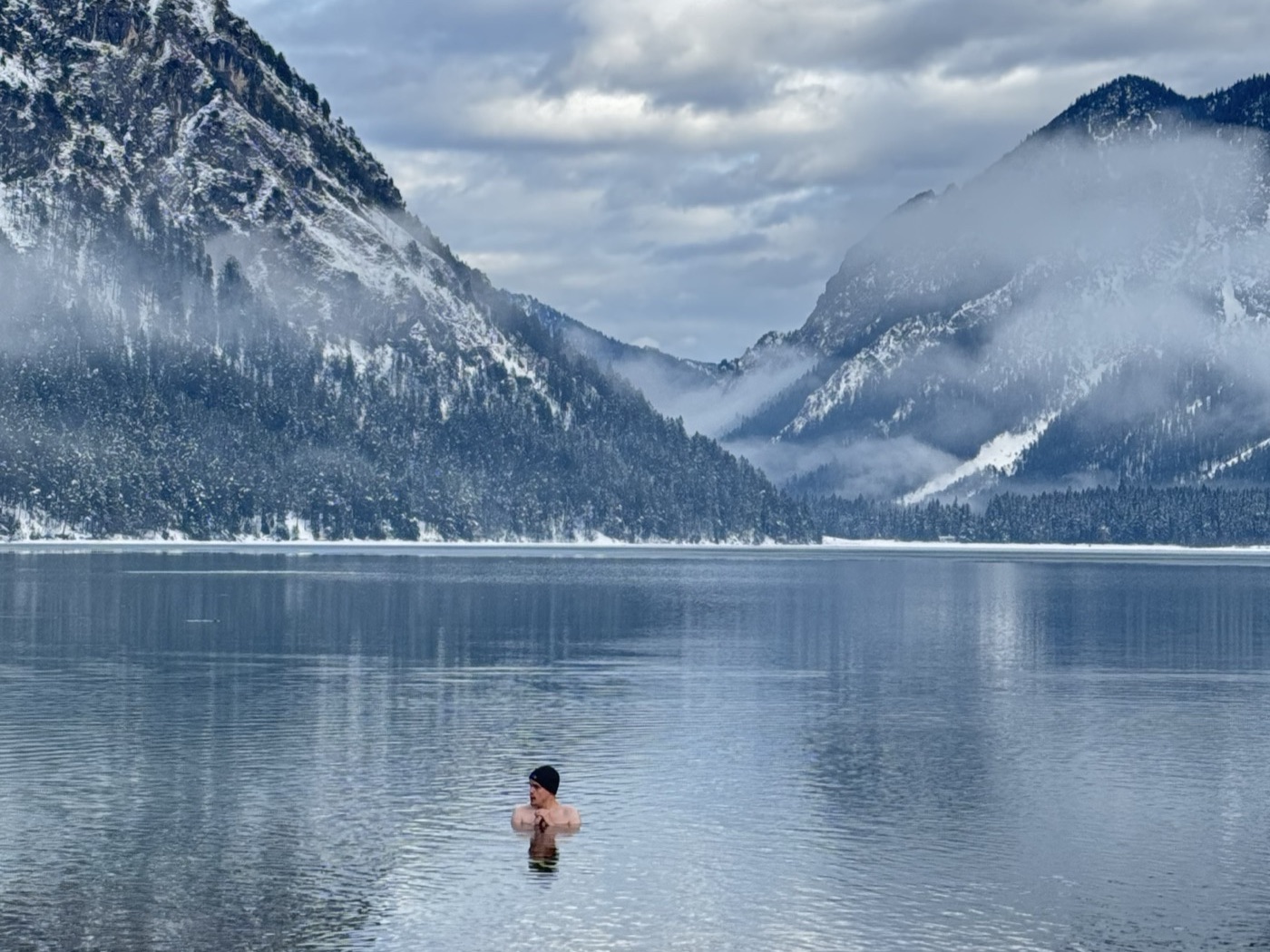Cold-water swimmer in Lake Heiterwang below snowy mountains