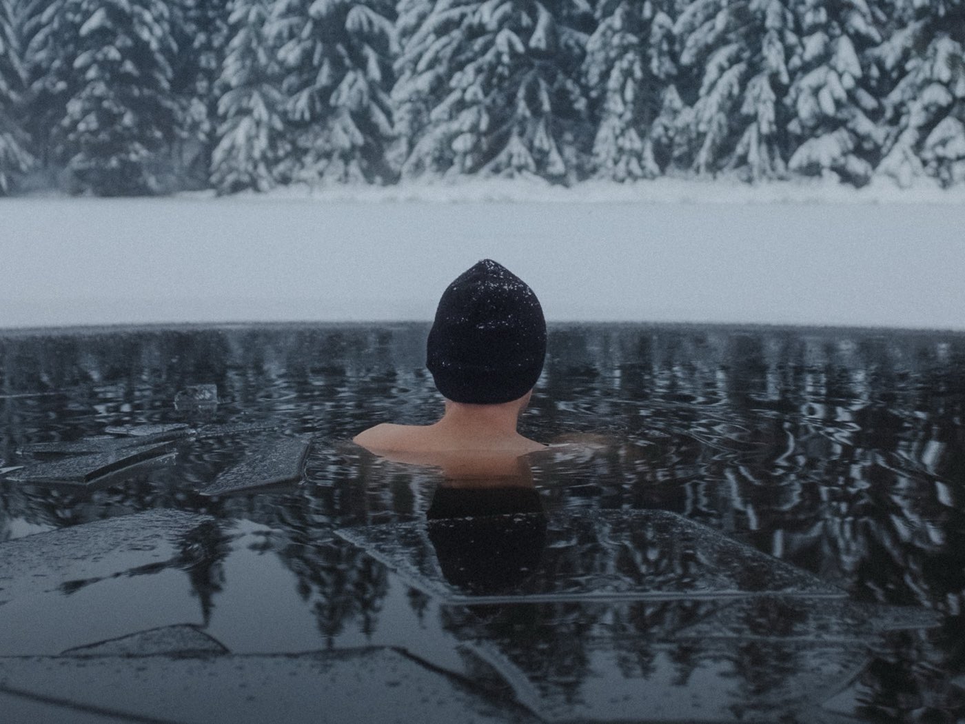 Ice bather in an ice hole in front of a snowy spruce forest